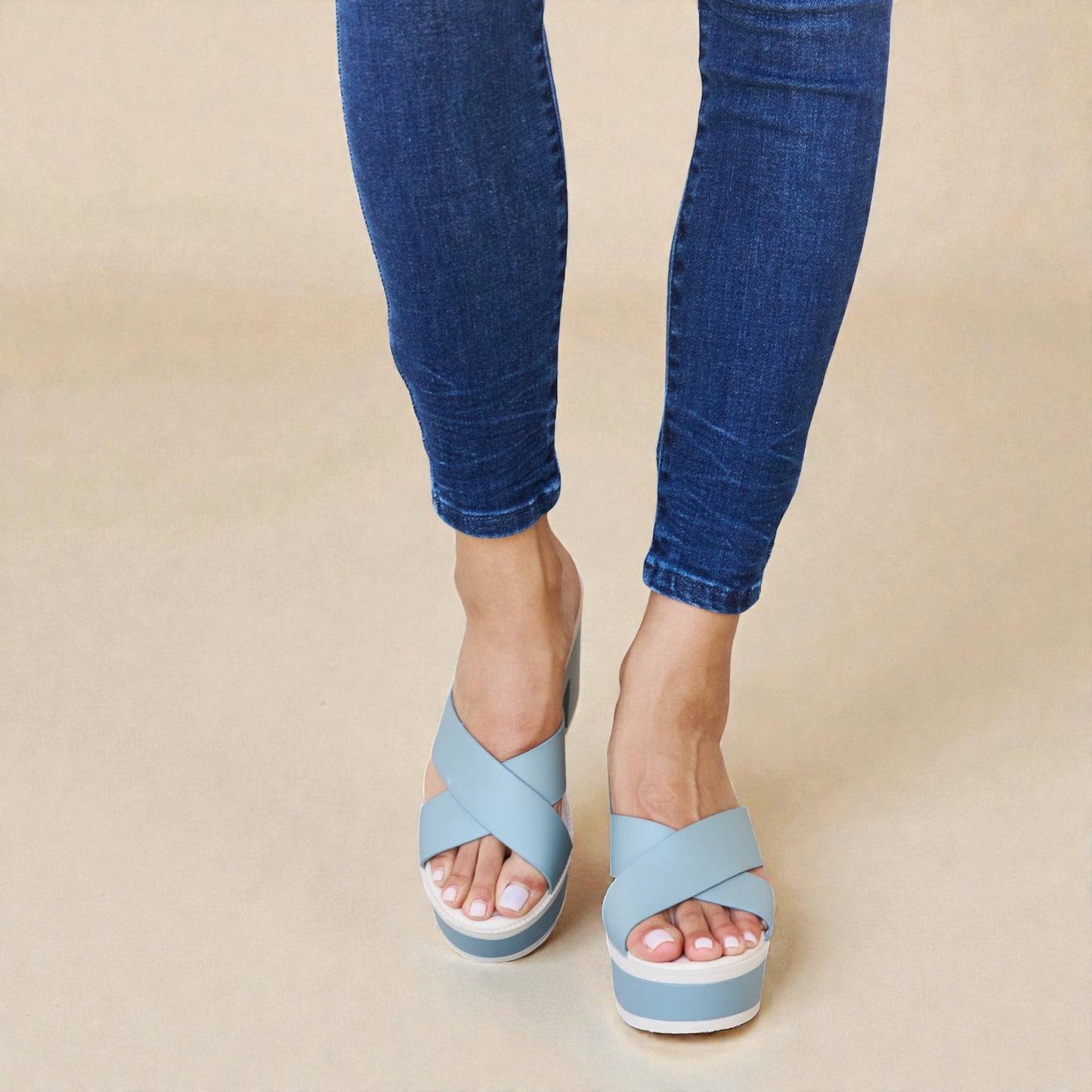 Blue sandals worn with blue jeans on a beige background