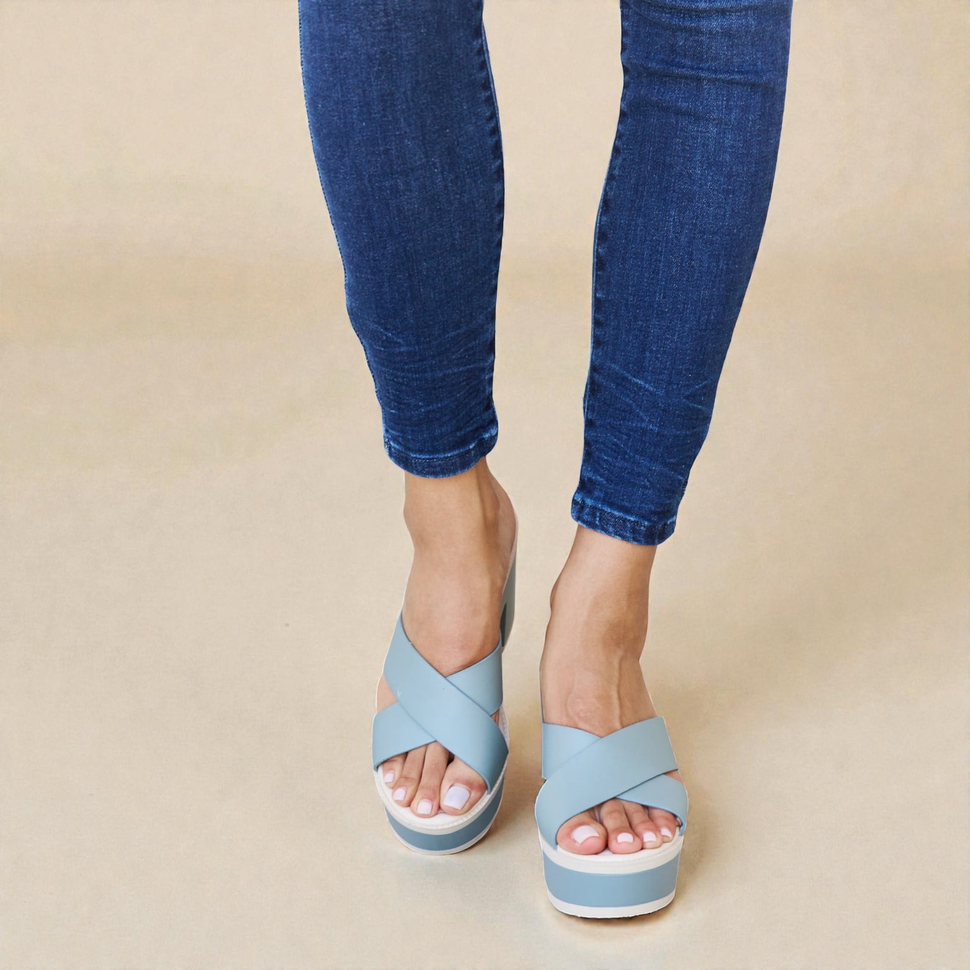 Blue sandals worn with blue jeans on a beige background