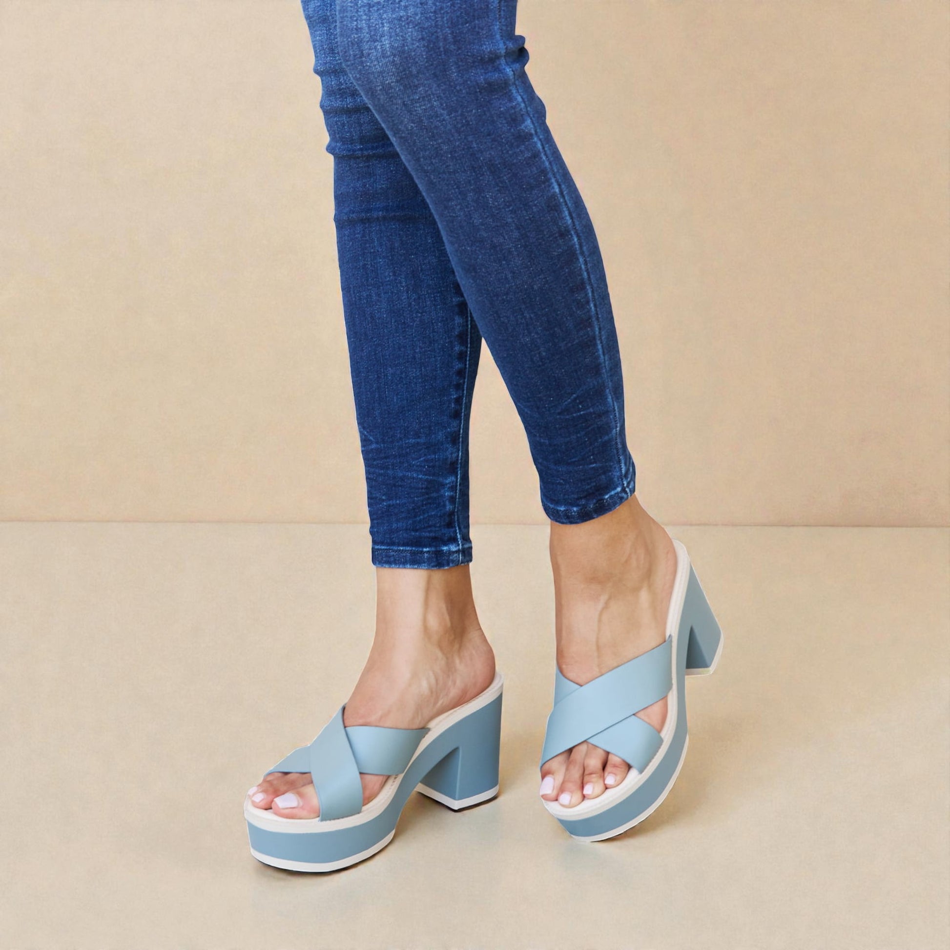 Light blue platform sandals worn with blue jeans on a beige background