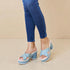 Light blue platform sandals worn with blue jeans on a beige background