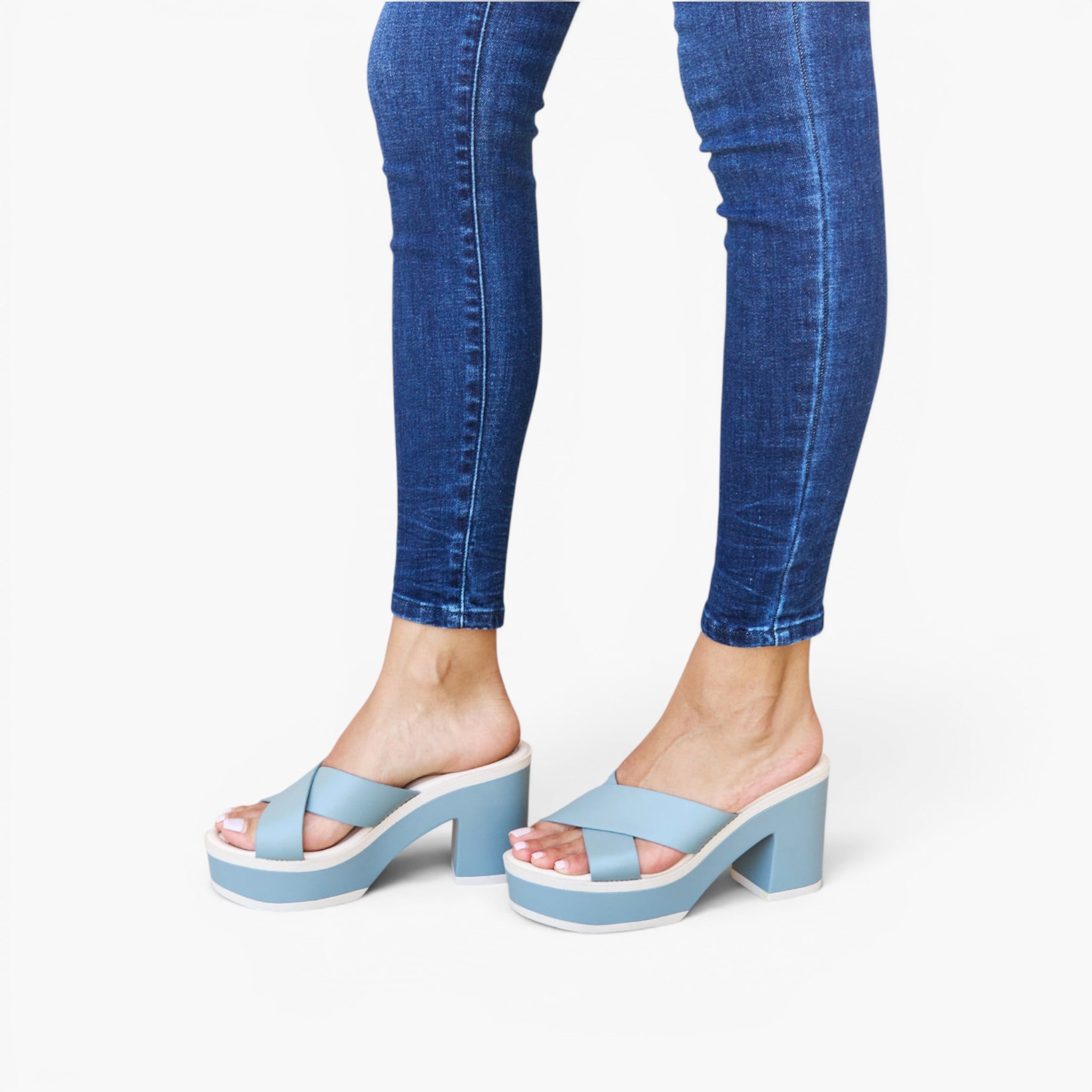 A person wearing light blue platform slide sandals with matching blue straps and blue skinny jeans, shown from the calves down against a plain white studio background.