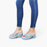A person wearing light blue platform slide sandals with matching blue straps and blue skinny jeans, shown from the calves down against a plain white studio background.