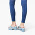 A person wearing blue skinny jeans and light blue platform slide sandals with chunky block heels, shown from the back against a plain white studio background.
