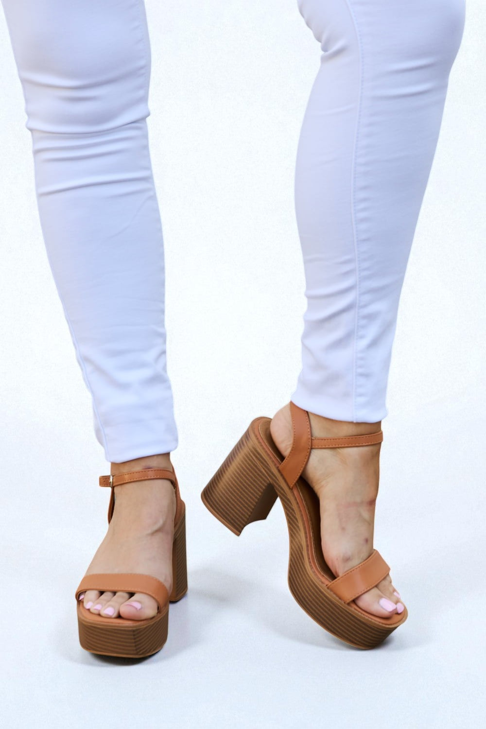 Brown platform sandals worn with white pants on a light background