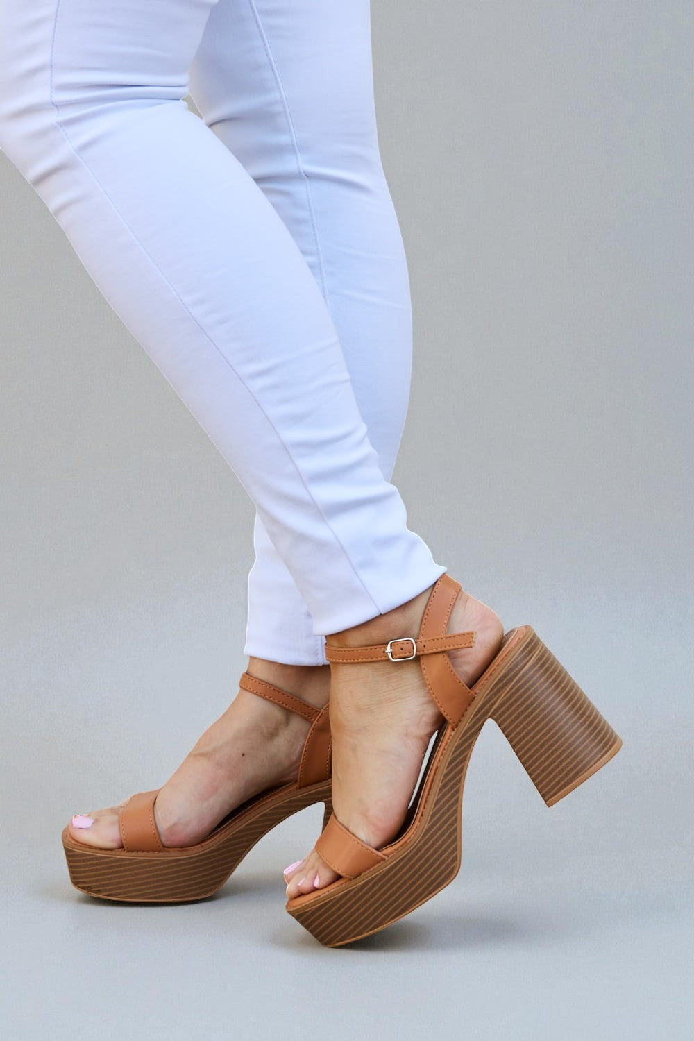 Brown platform sandals worn with white pants on a gray background