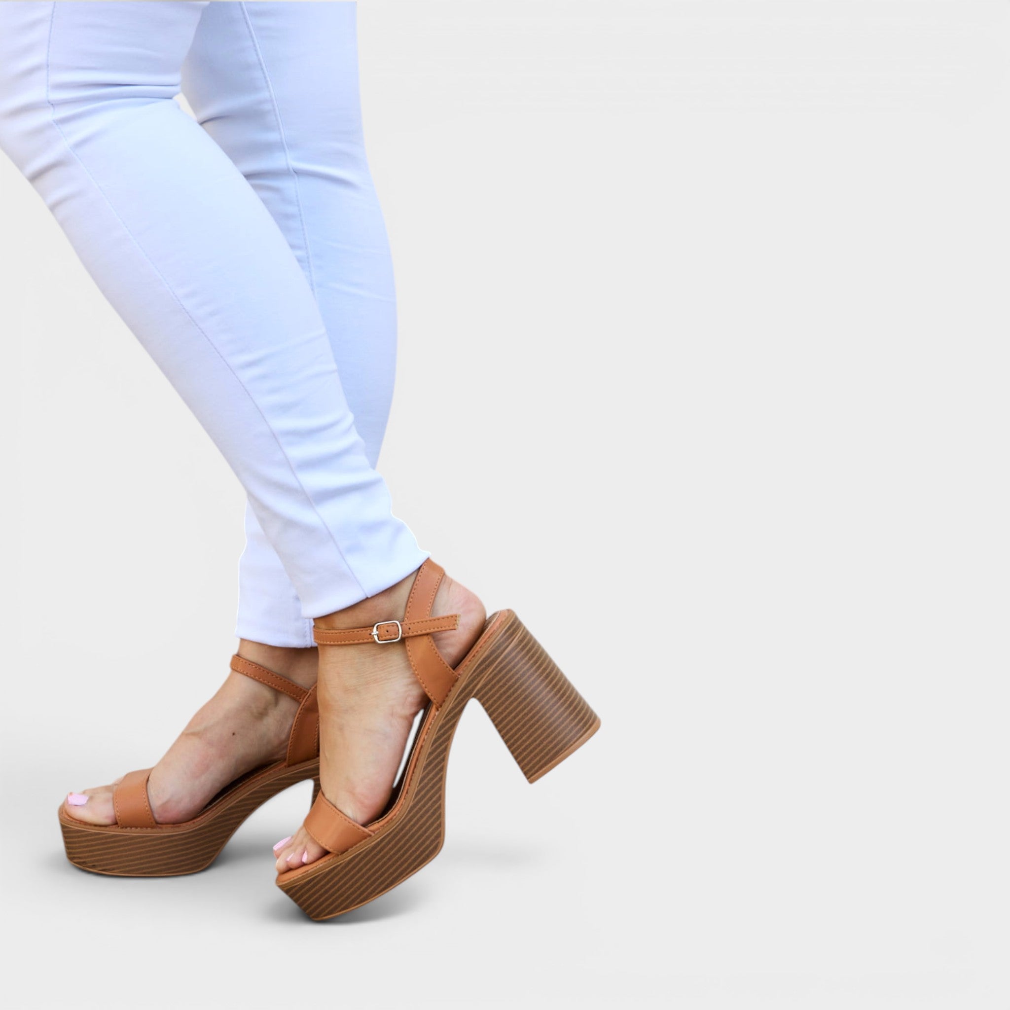 Brown platform sandals worn with white pants on a light gray background