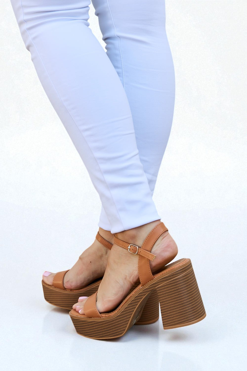 Brown platform sandals worn with white pants on a white background