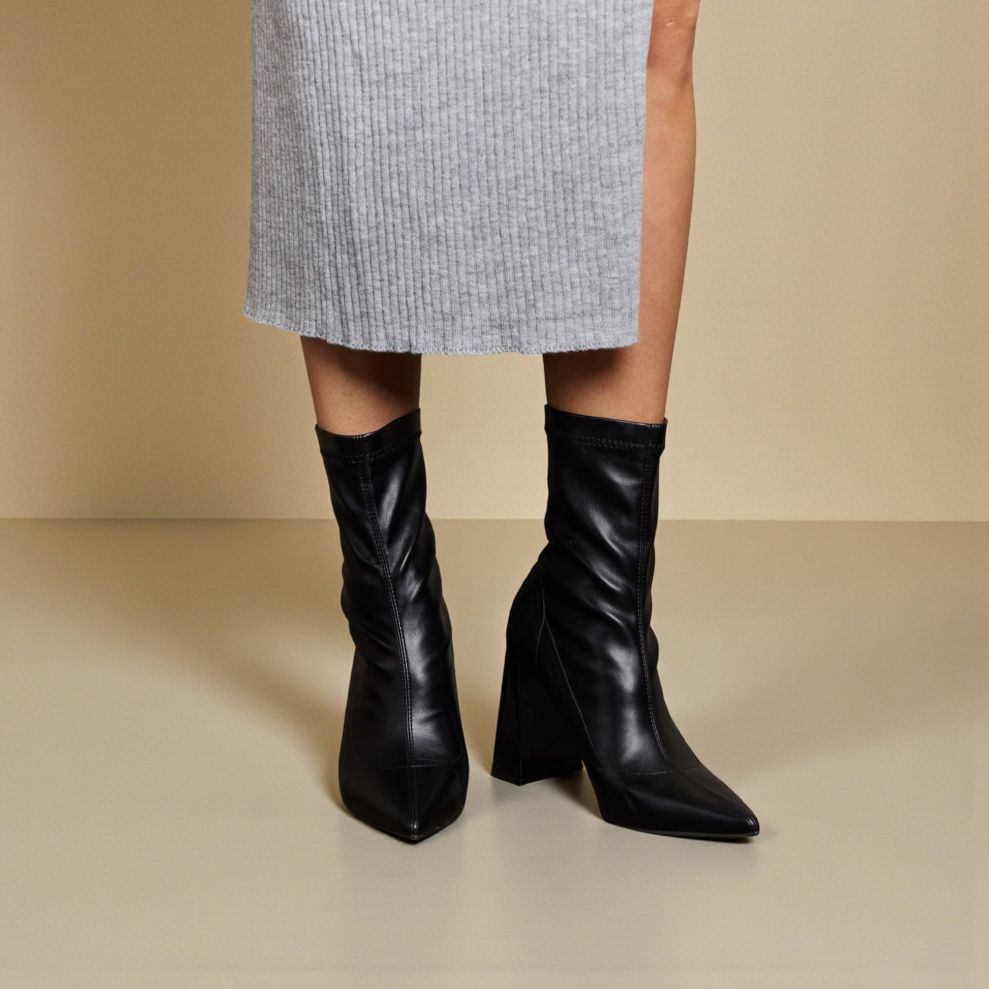 Black knee-high boots worn with a gray skirt on a beige background