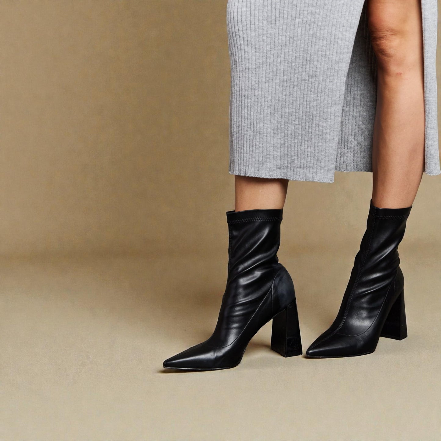 Black knee-high boots worn with a gray skirt on a beige background