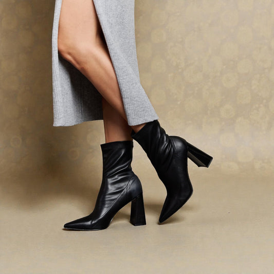 Black ankle boots worn with a gray skirt on a beige background