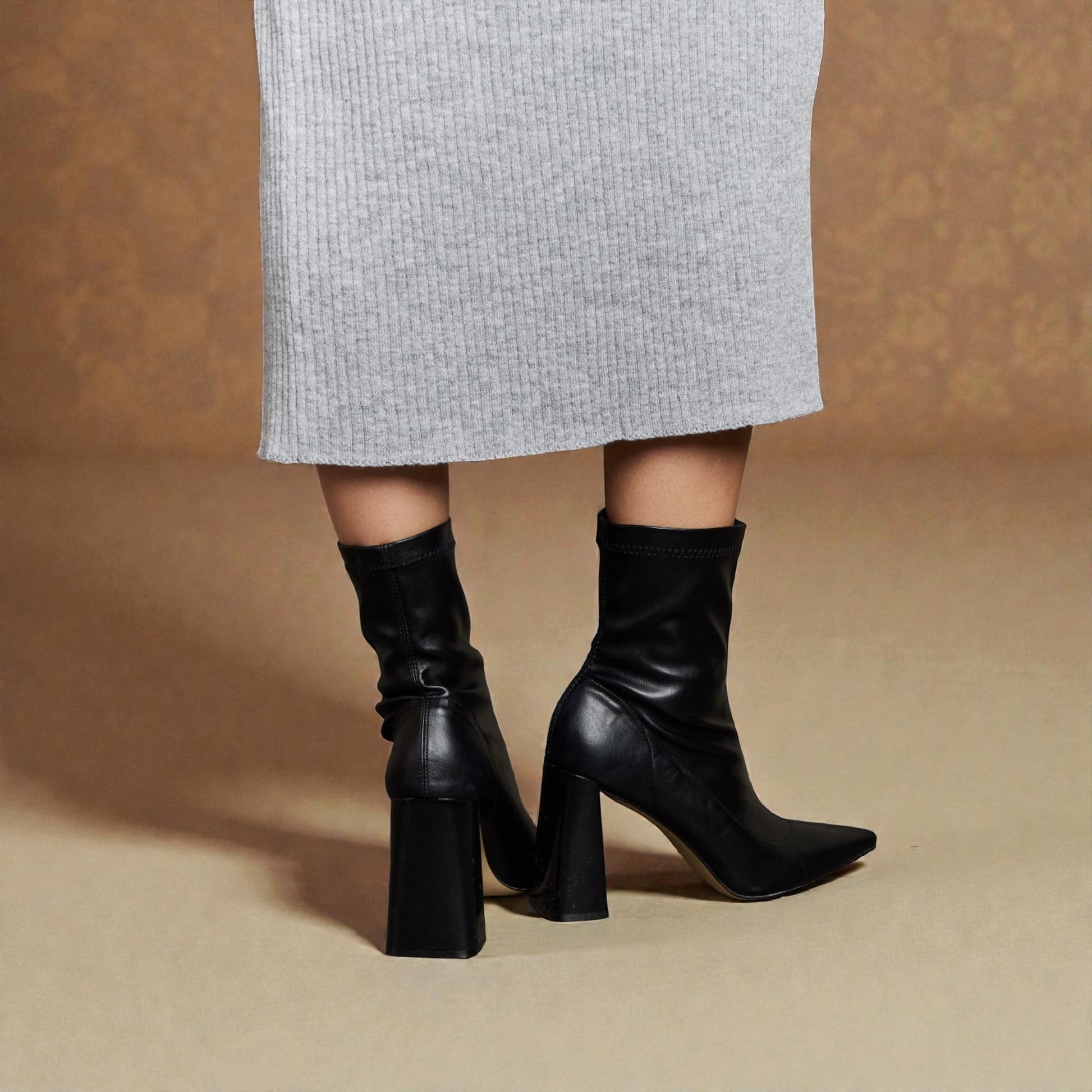 Black knee-high boots worn with a gray skirt on a beige background