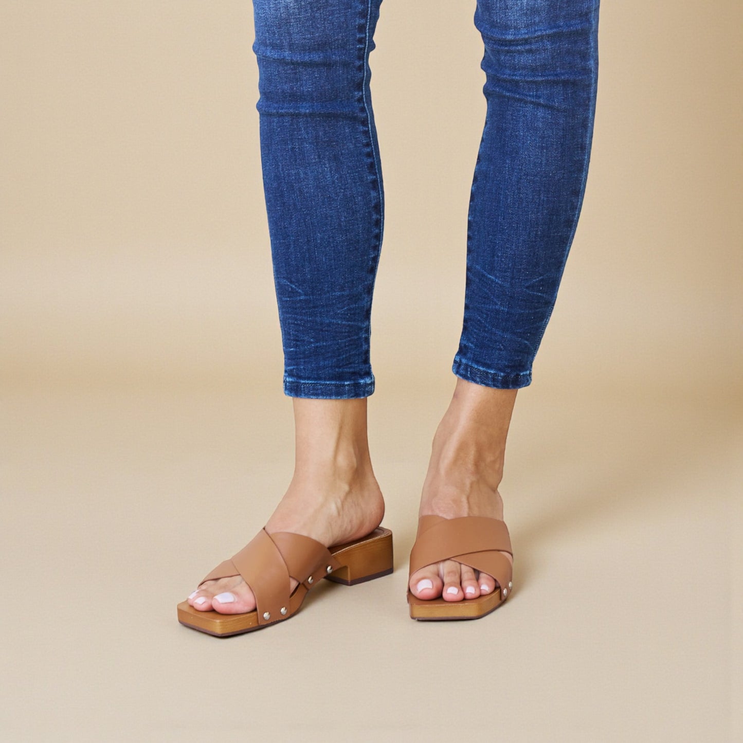 Person wearing blue jeans and brown sandals on a beige background