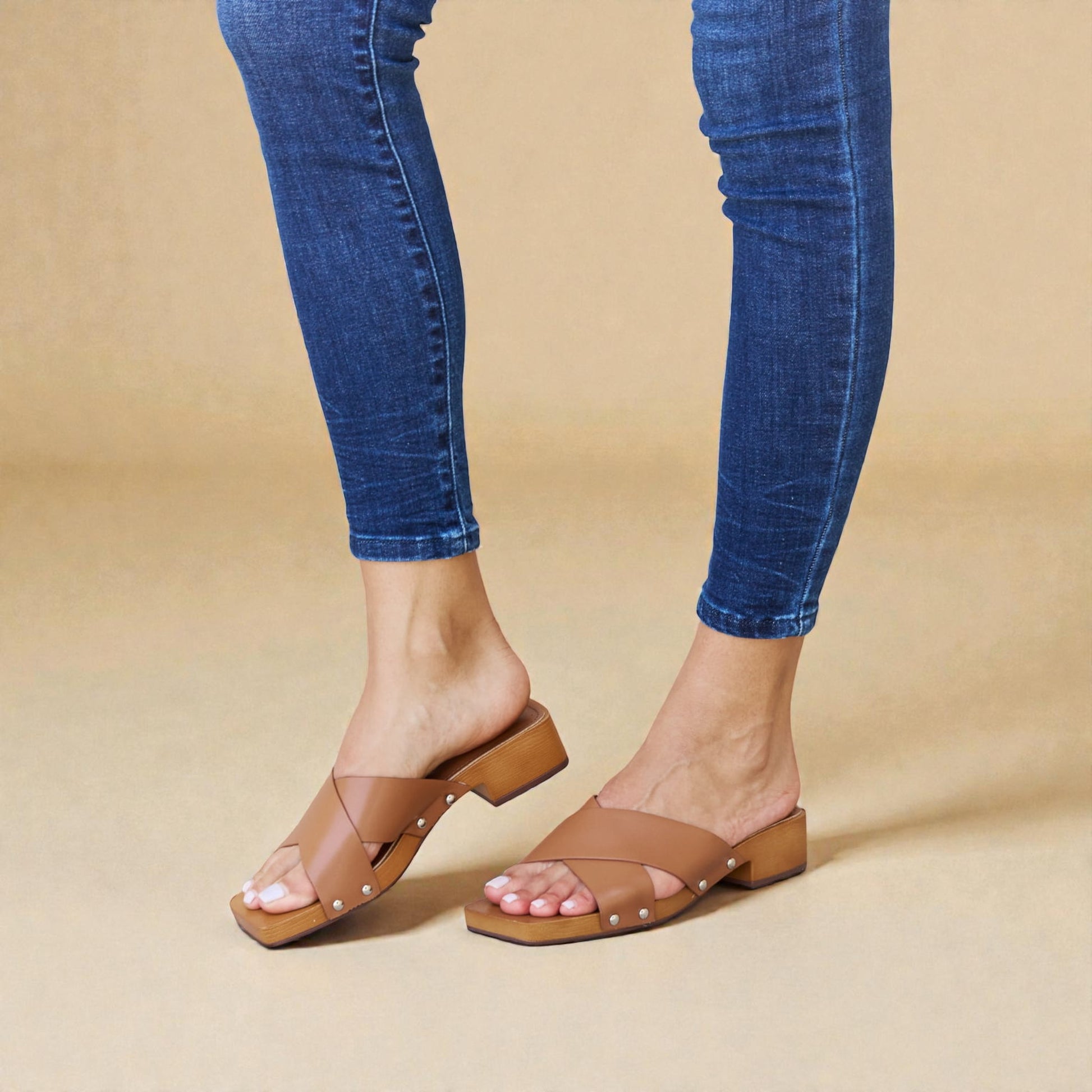 Person wearing brown sandals and blue jeans on a beige background