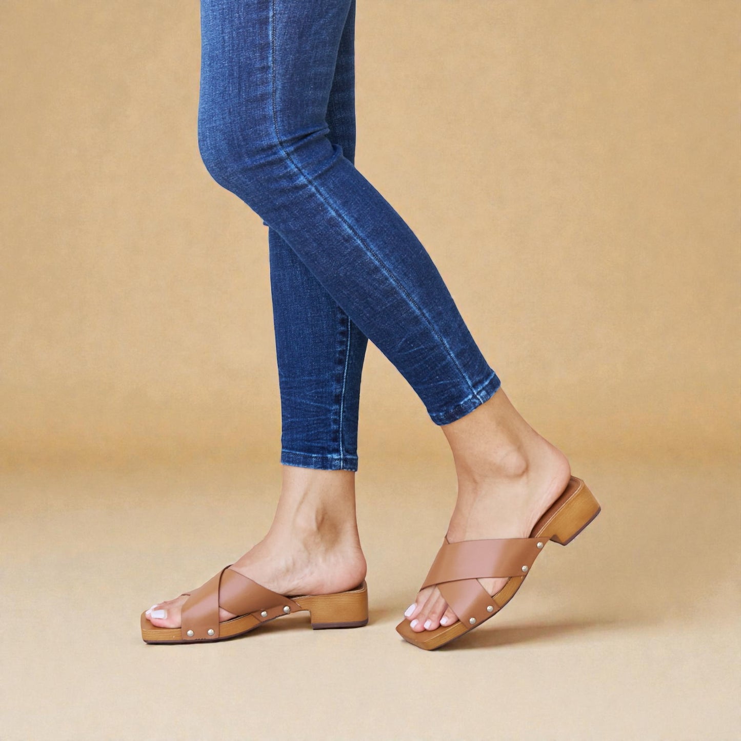 Person wearing blue jeans and brown sandals on a beige background