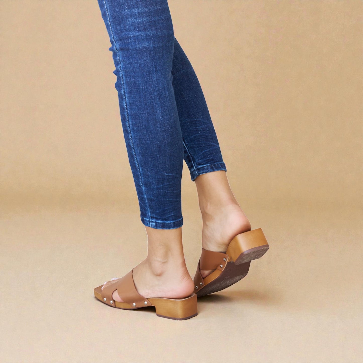 Person wearing blue jeans and brown sandals on a beige background