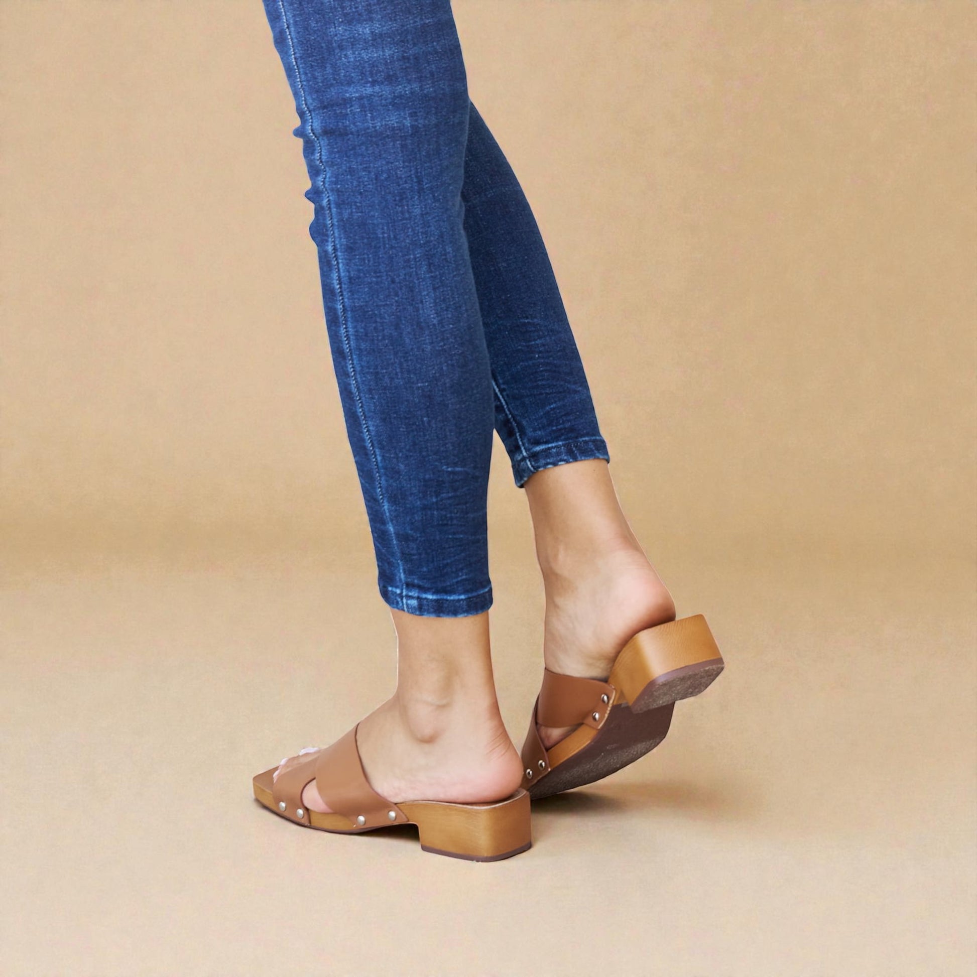 Person wearing blue jeans and brown sandals on a beige background