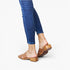 A person wearing blue skinny jeans and brown leather slide sandals with small silver studs, shown from the calves down against a clean white studio background.