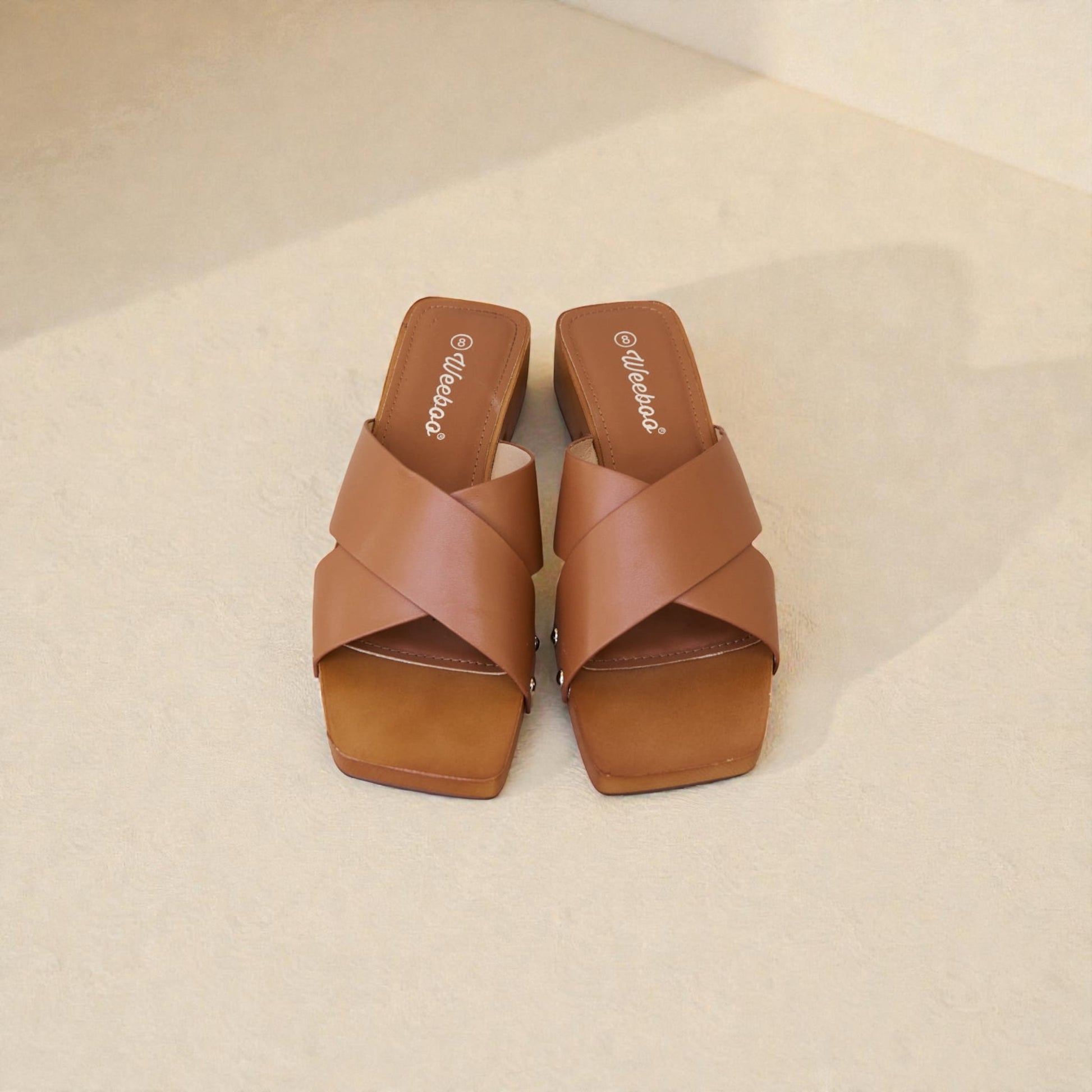 Pair of brown sandals with criss-cross design on a beige background