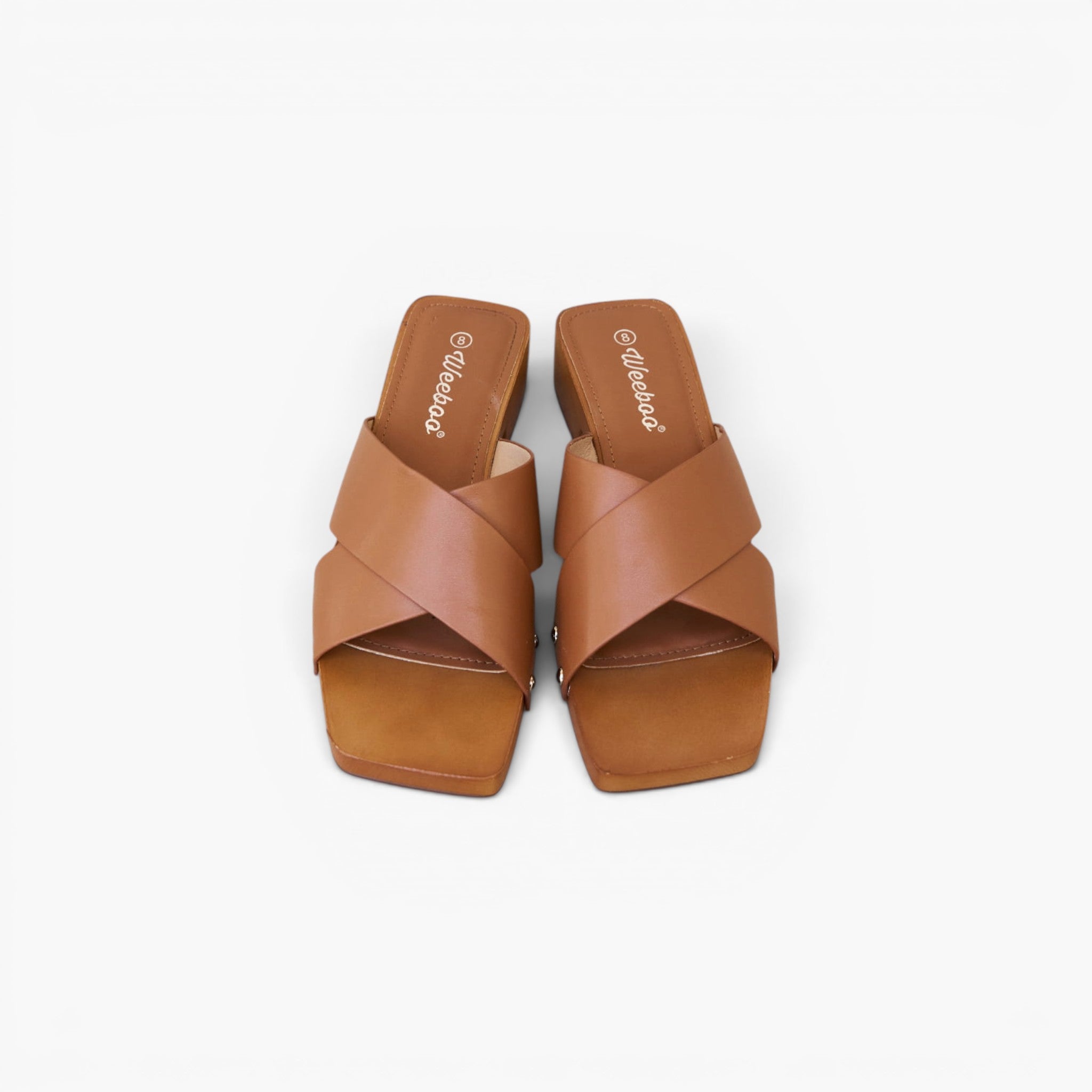 A pair of tan leather slide sandals with wide crisscross straps and low block heels, shown from a top-down view on a light gray background.