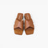 A pair of tan leather slide sandals with wide crisscross straps and low block heels, shown from a top-down view on a light gray background.
