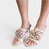 Beige open-toe heeled sandals with large fabric rose embellishments on the front, shown on a model's feet against a light gray background.