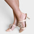 Beige strappy heeled sandals with ruffled floral details on the straps, shown on a model's feet against a light gray background.