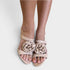 Beige open-toe heeled sandals with large fabric flower embellishments on the front, shown worn on a model's feet against a light gray background.