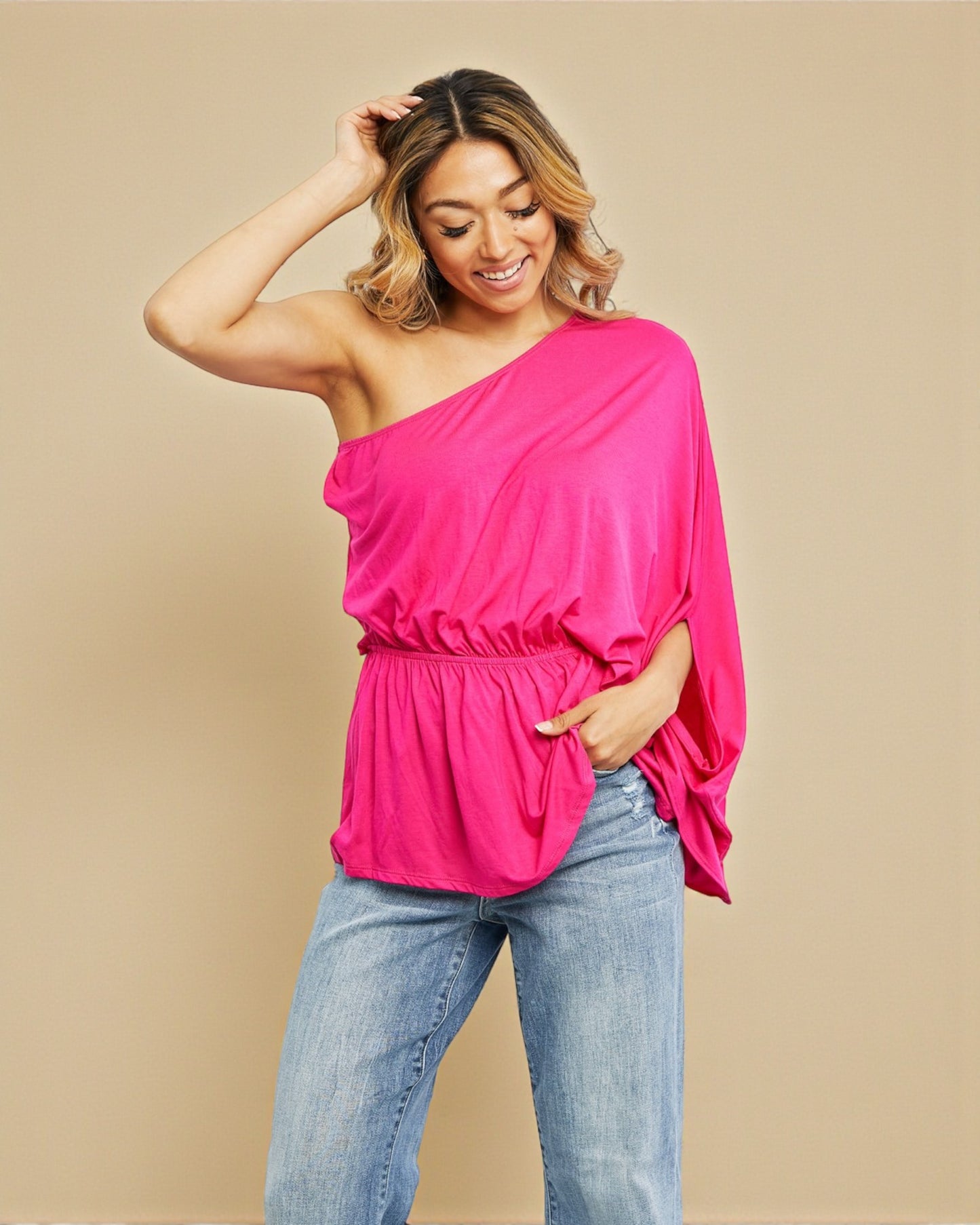 Woman wearing a bright pink one-shoulder top and blue jeans on a beige background