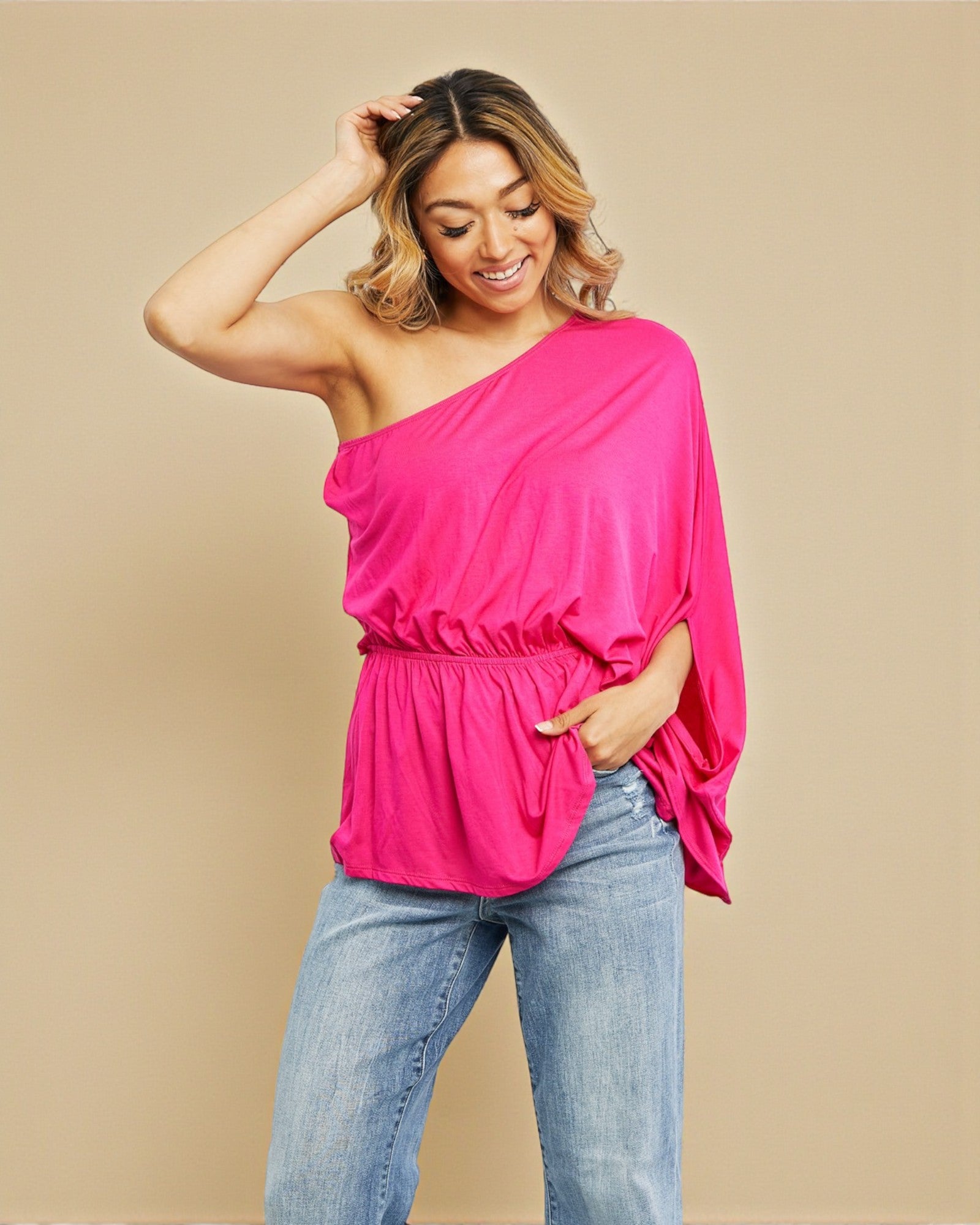 Woman wearing a bright pink one-shoulder top and blue jeans on a beige background