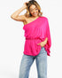 A woman modeling a bright pink one-shoulder draped top with a gathered waist, paired with light-wash blue jeans, against a plain white background.