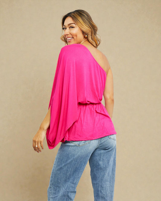 Woman wearing a bright pink one-shoulder top and blue jeans on a beige background