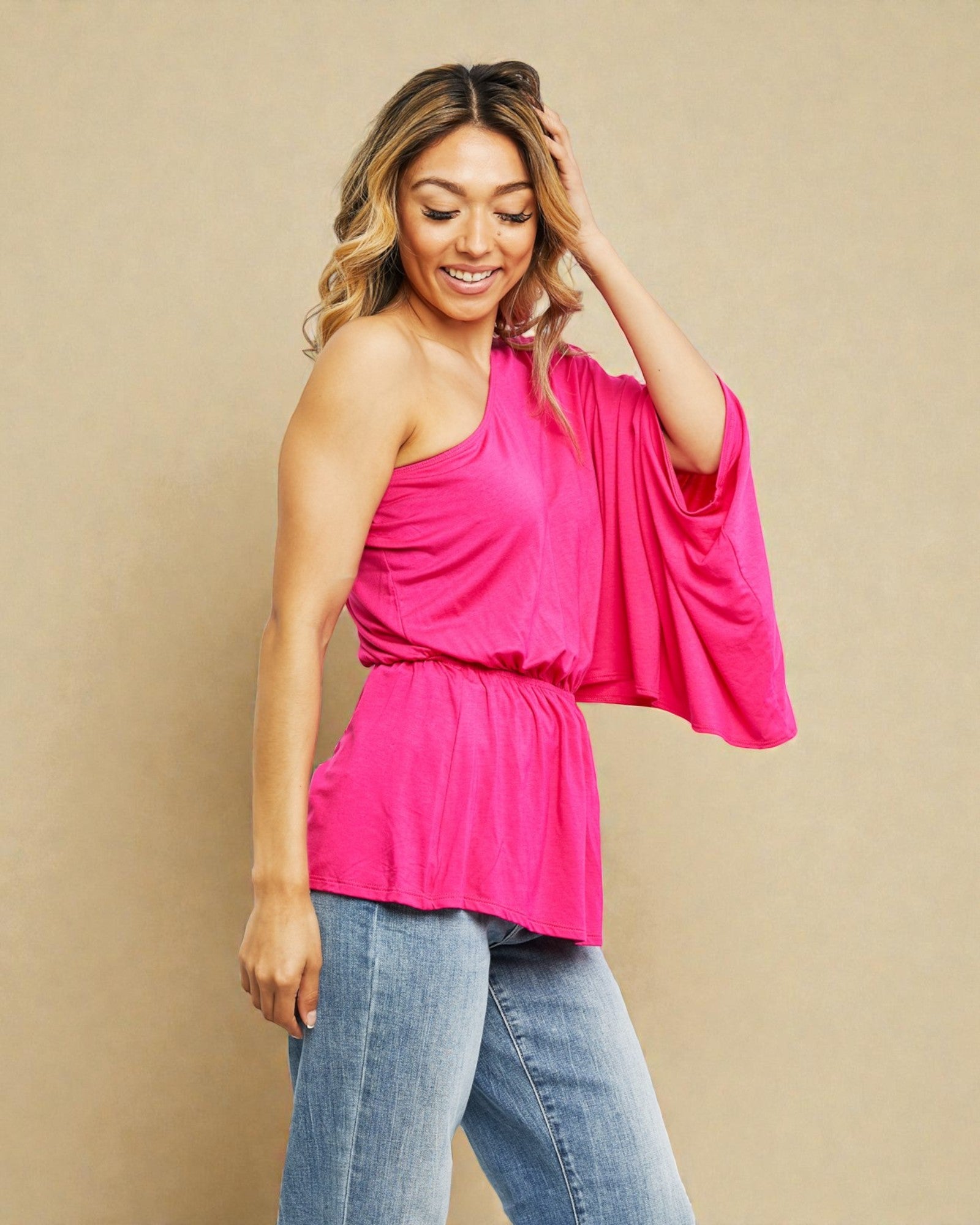 Woman wearing a bright pink one-shoulder top and blue jeans on a beige background