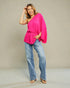 Woman wearing a bright pink top and blue jeans against a plain background