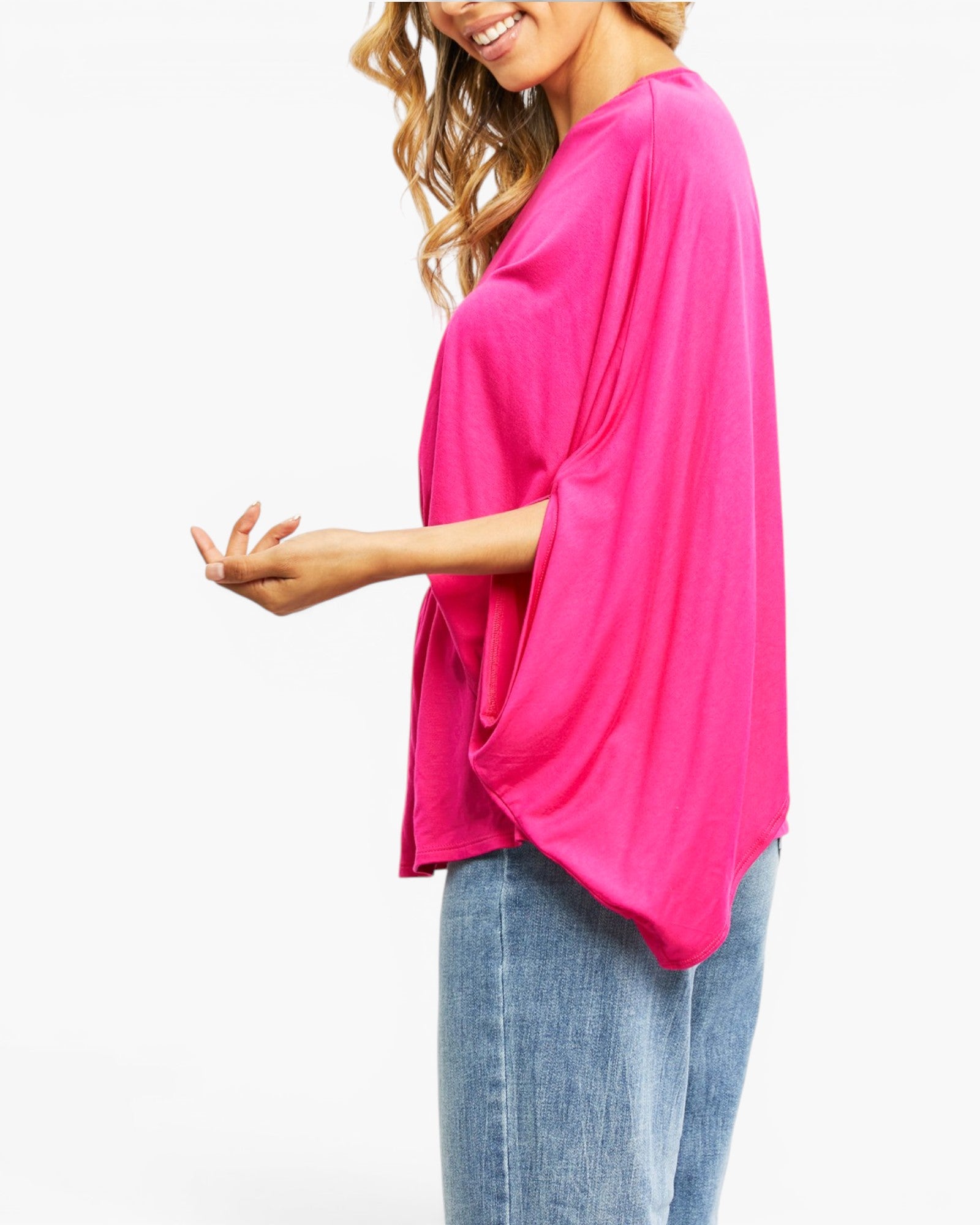 A woman wearing a bright pink, loose-fitting short-sleeve top with wide draped sleeves and light blue jeans, shown from a side profile against a plain white background.