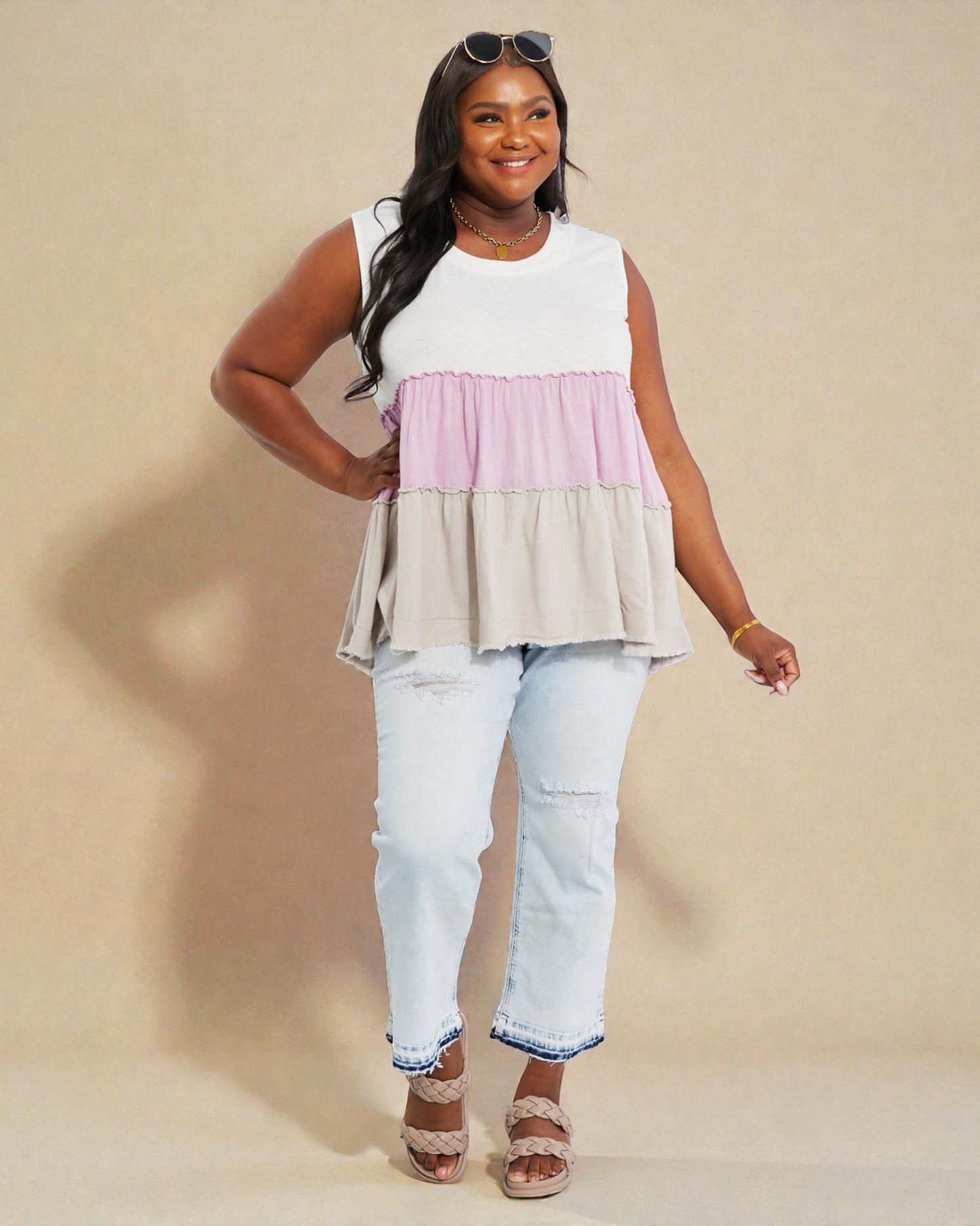 Woman wearing a layered sleeveless top and jeans on a beige background