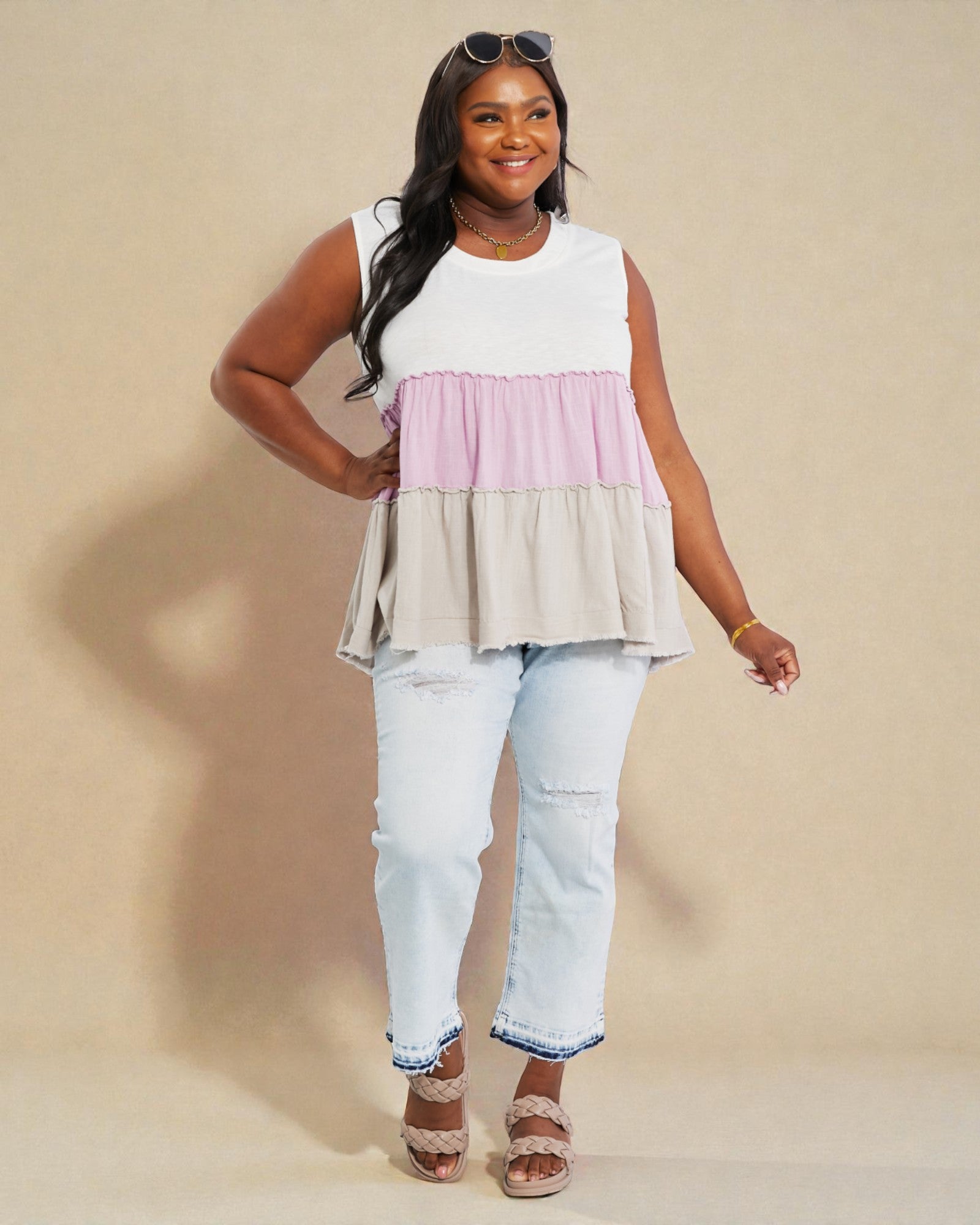 Woman wearing a layered sleeveless top and jeans on a beige background