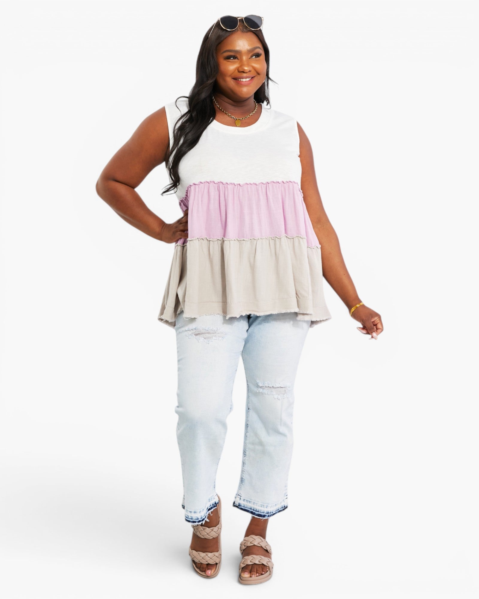 A woman modeling a sleeveless tiered peplum top with horizontal color-blocked panels in white, light pink, and light beige, paired with light-wash distressed jeans and brown sandals against a plain white studio background.