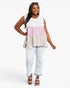 A woman modeling a sleeveless tiered peplum top with horizontal color-blocked panels in white, light pink, and light beige, paired with light-wash distressed jeans and brown sandals against a plain white studio background.