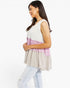 A woman wearing a sleeveless tiered tunic top with color-blocked sections of white, dusty pink, and light beige, paired with light-wash jeans, photographed against a solid white background.