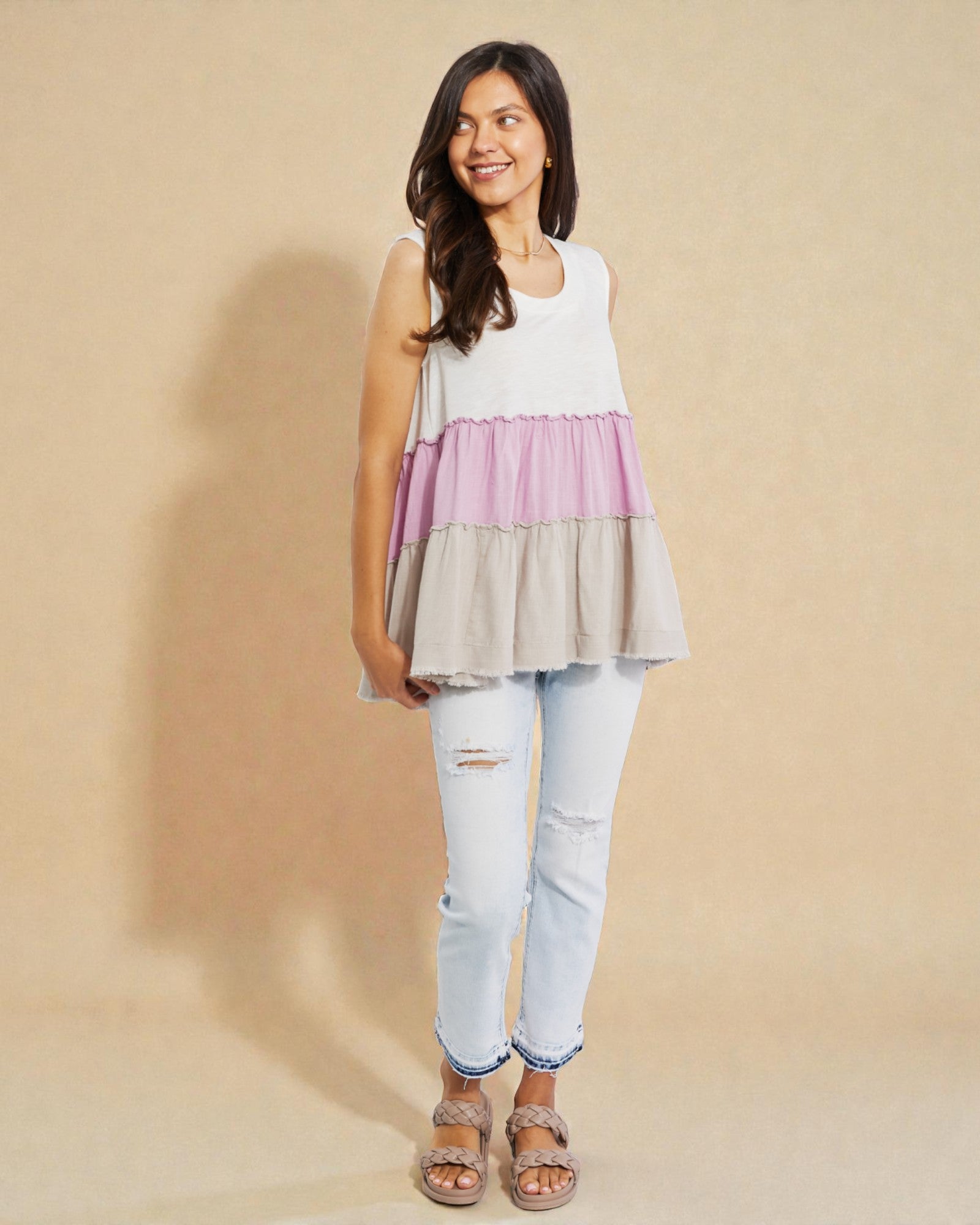 Woman wearing a layered sleeveless top and light blue jeans on a beige background