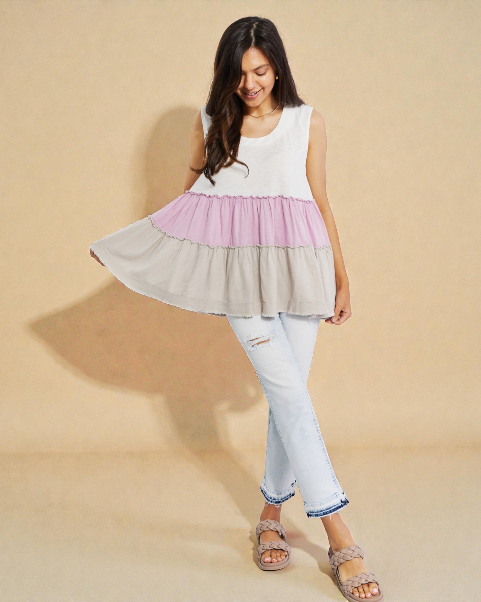 Woman wearing a layered dress with a white top, pink middle, and beige bottom on a beige background