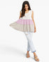 A woman modeling a sleeveless tiered tunic top with a white upper section, a light pink middle band, and a light beige flared lower skirt, paired with light-wash jeans and sandals on a white studio background.