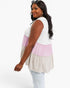 A woman wearing a sleeveless tiered tunic top with color-blocked sections of white, light pink, and light beige, paired with light-wash jeans against a plain white studio background.