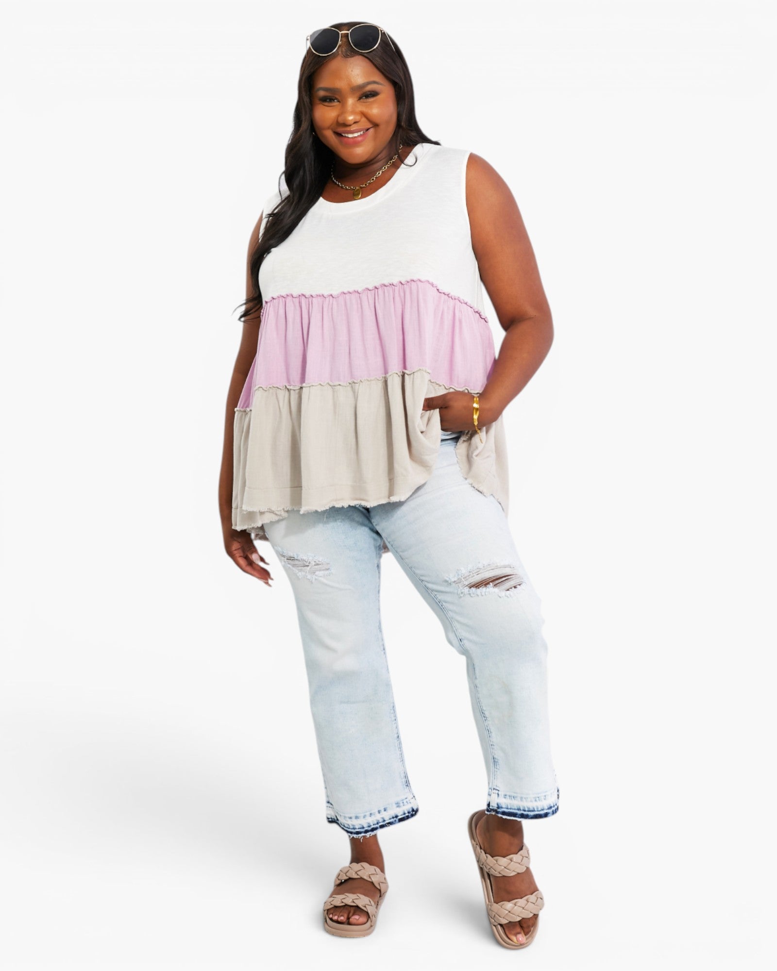A woman modeling a sleeveless tiered colorblock top with white, light pink, and beige horizontal panels, paired with light-wash distressed jeans and brown wedge sandals against a plain white studio background.