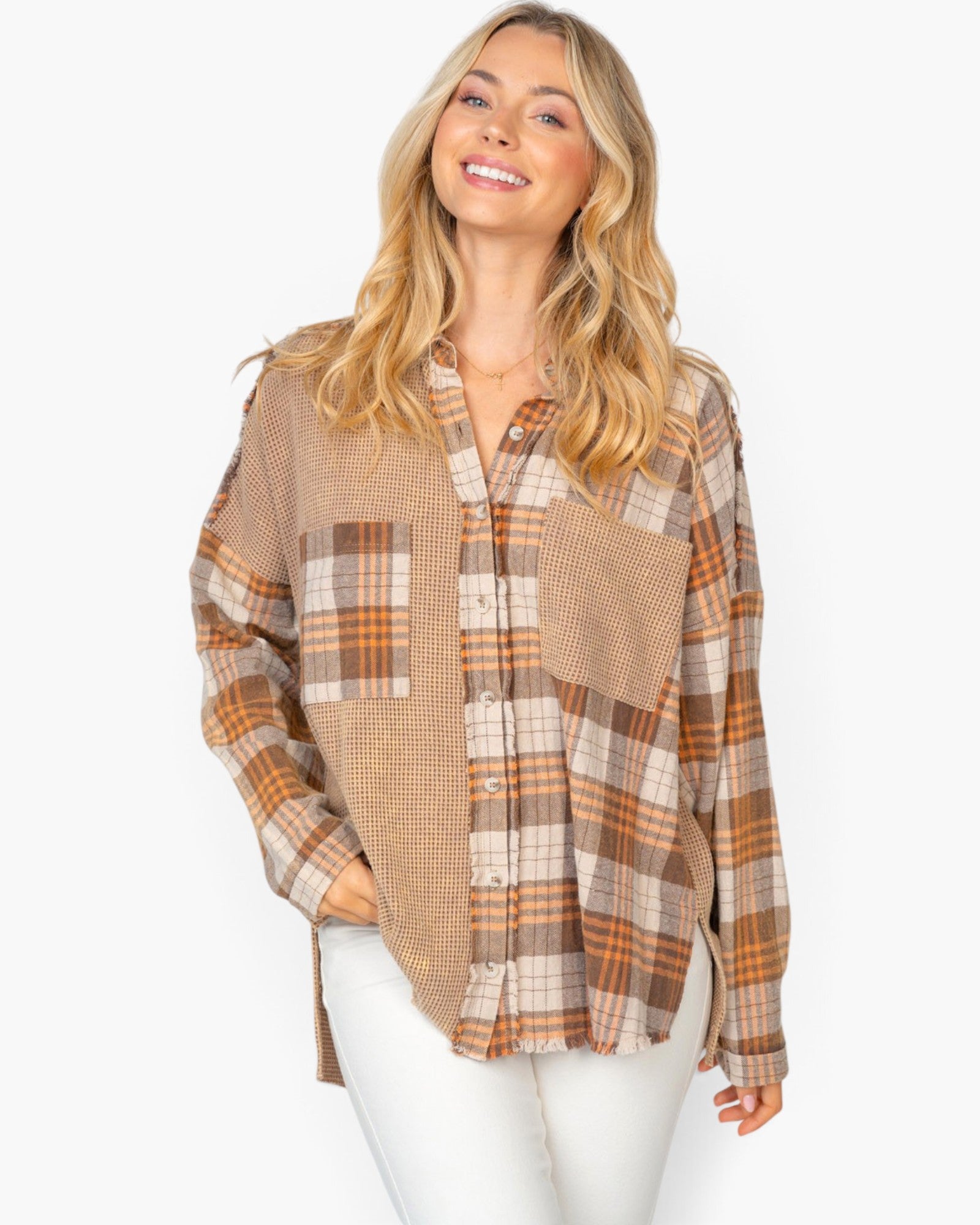 A woman wearing a long-sleeve button-up shirt with a mixed plaid pattern in beige, brown, and orange, paired with white pants, against a plain white background.