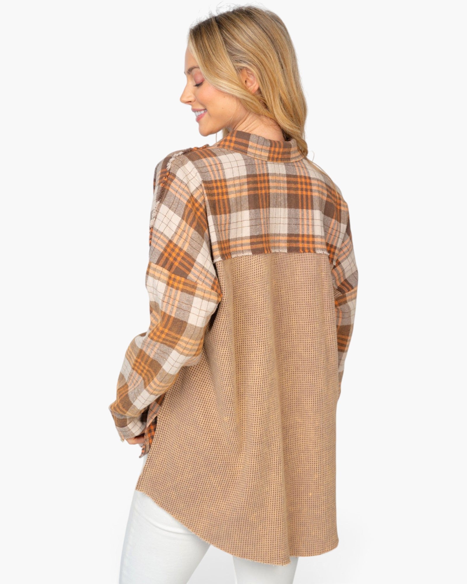 A woman shown from the back wearing a color-block plaid shirt with a brown and beige plaid upper back and shoulders, and a solid tan textured lower back panel, paired with white pants against a light gray background.