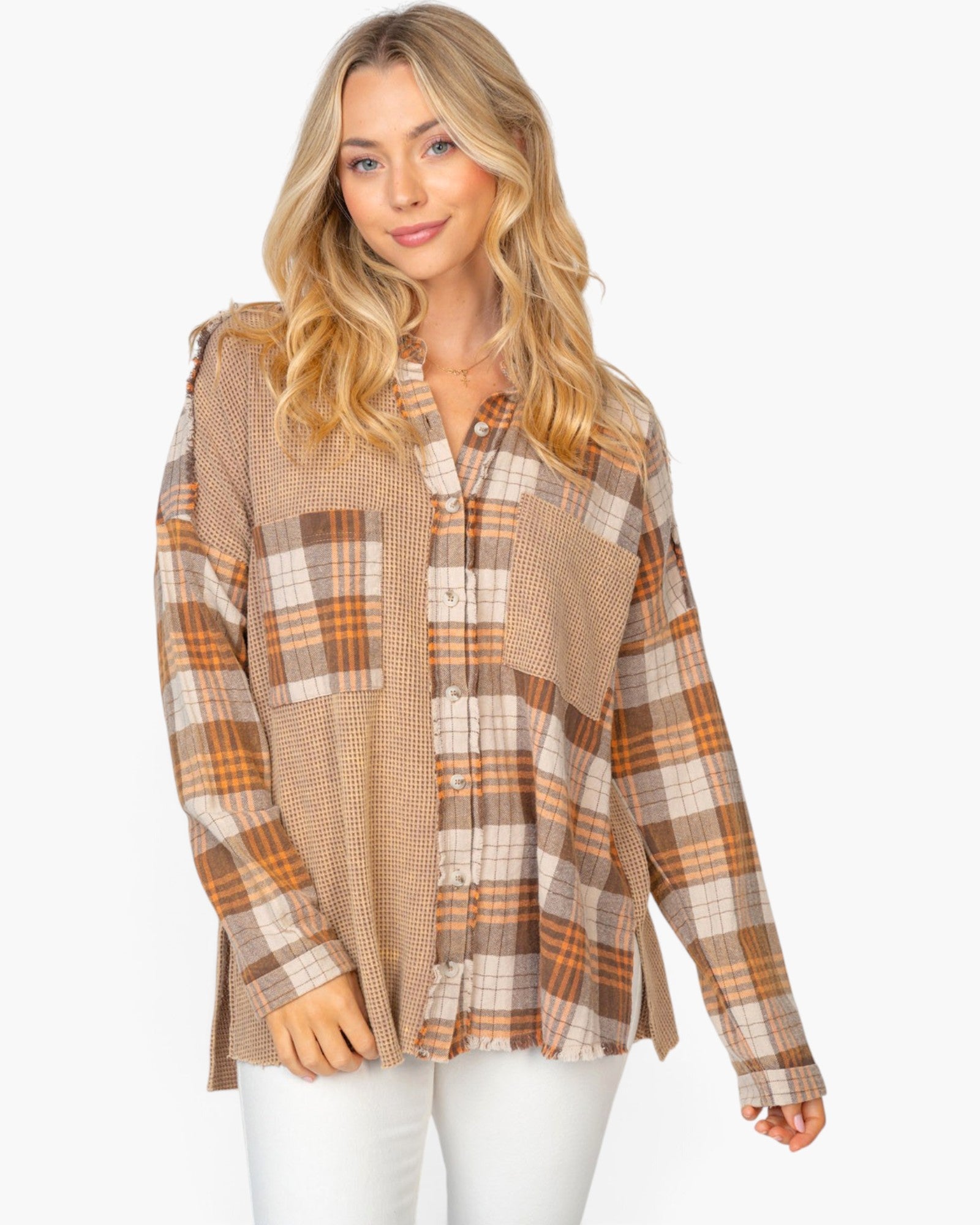 A woman modeling a long-sleeve patchwork button-up shirt in beige, brown, and orange plaid, paired with white pants against a light gray background.