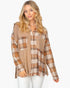 A woman modeling a long-sleeve patchwork button-up shirt in beige, brown, and orange plaid, paired with white pants against a light gray background.