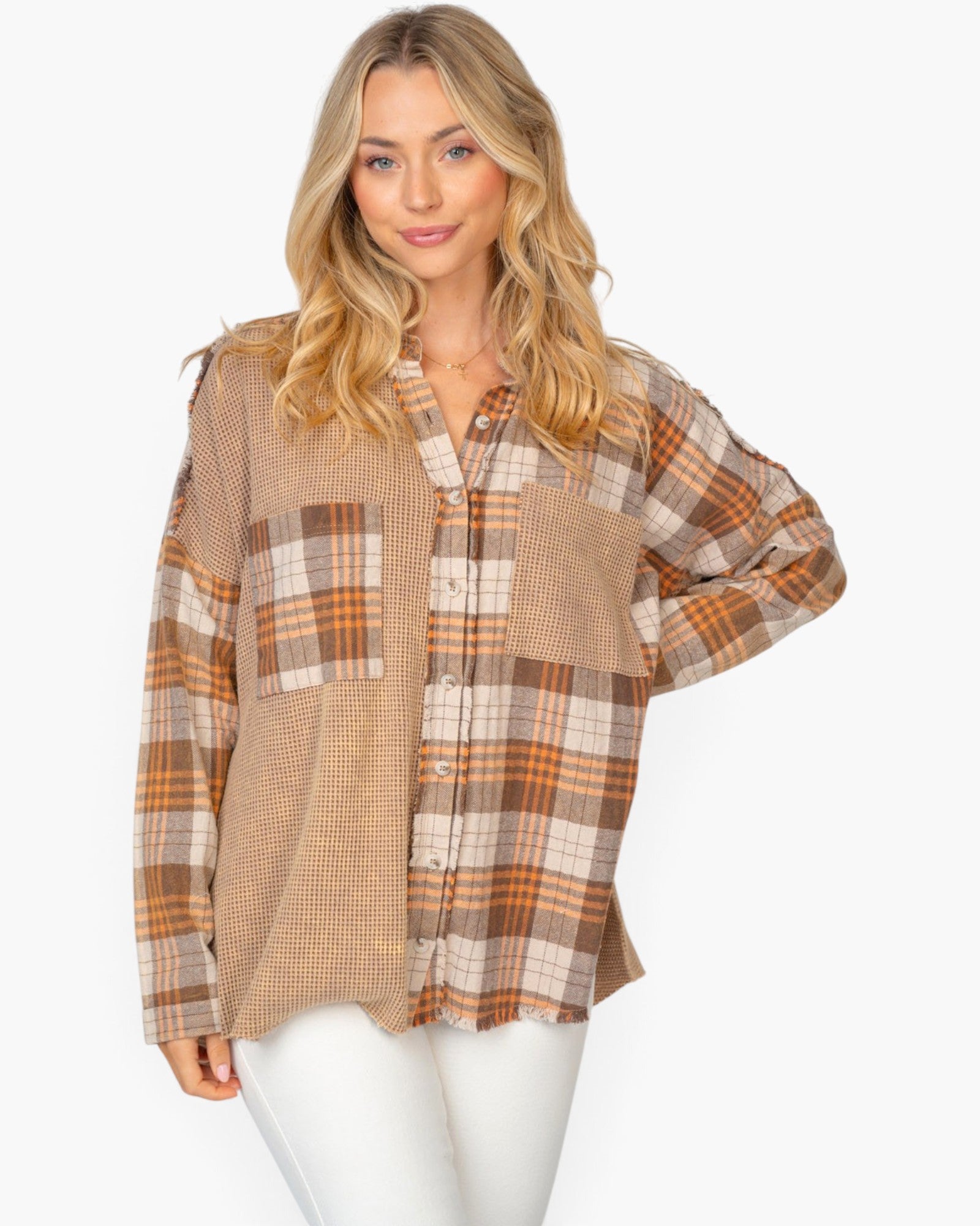 A woman modeling a long-sleeve patchwork button-up shirt in beige, brown, and orange plaid patterns, paired with white pants, against a plain white background.