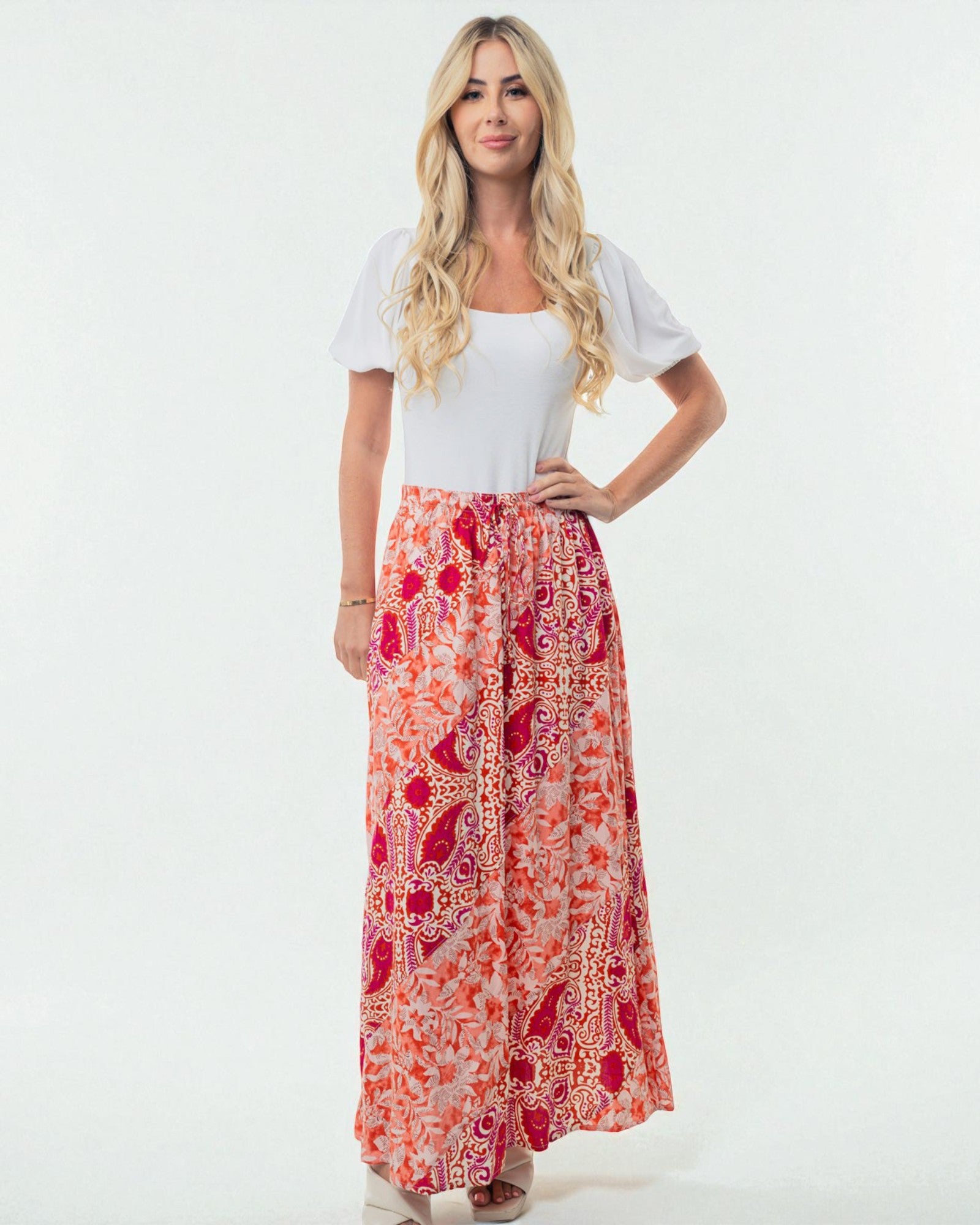 Woman wearing a white top and a long, patterned orange and red skirt on a white background